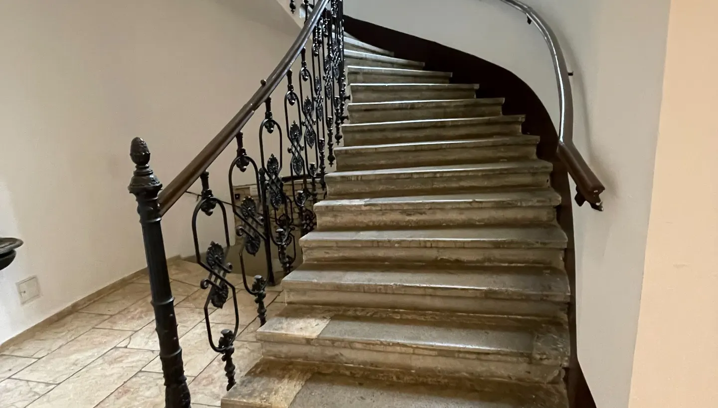 Geschwungene historische Treppe mit schmiedeeisernem Geländer.