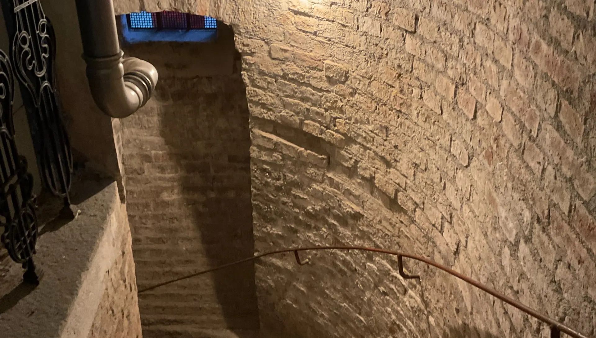 Gewölbter Ziegelkeller mit Treppe und Leitungen.