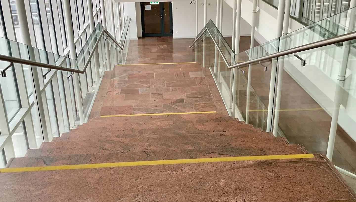 Treppenanlage mit Glasbrüstungen und Steinboden in einem Bürogebäude.