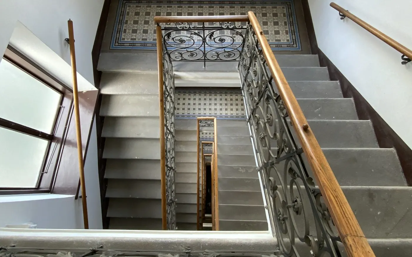Blick von oben in ein Altbau-Stiegenhaus mit schmiedeeisernem Geländer und Holzhandlauf.