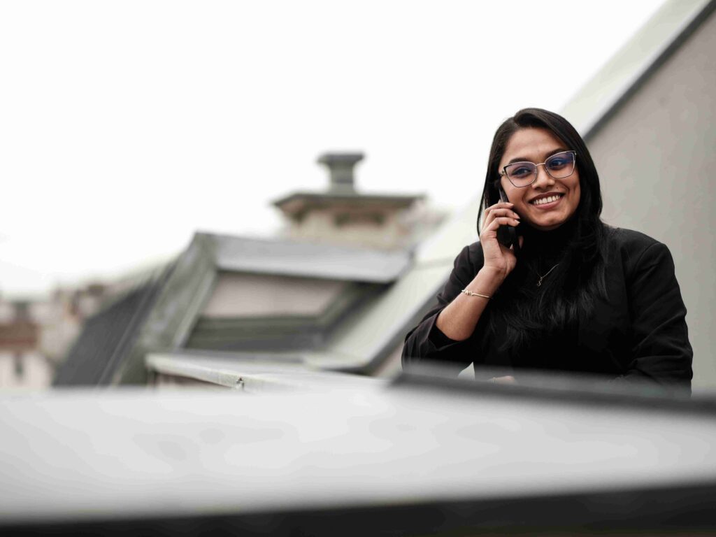 Eine l&auml;chelnde Projektleiterin der Themis Baumanagement w&auml;hrend eines Beratungsgespr&auml;chs am Telefon auf einer Dachterrasse.