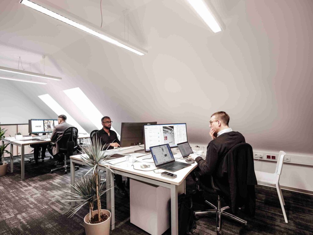 Drei Experten der Themis Baumanagement arbeiten konzentriert an modernen Computer-Arbeitsplätzen in einem hellen Dachgeschossbüro an der technischen Projektplanung.