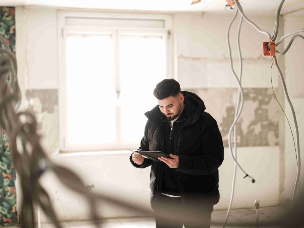 Ein Mitarbeiter von Themis steht in einer entkernten Altbauwohnung während Sanierungsarbeiten und trägt Daten in sein Tablet ein.